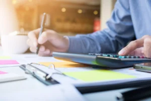 Persona calcula y anota datos financieros en un escritorio