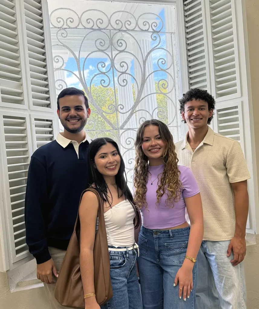 Cuatro jóvenes sonríen junto a ventana decorativa