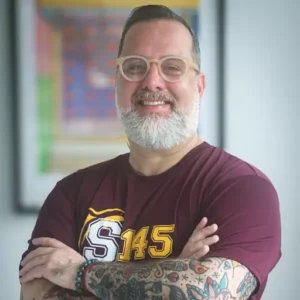 Hombre sonriente con barba y tatuajes, brazos cruzados